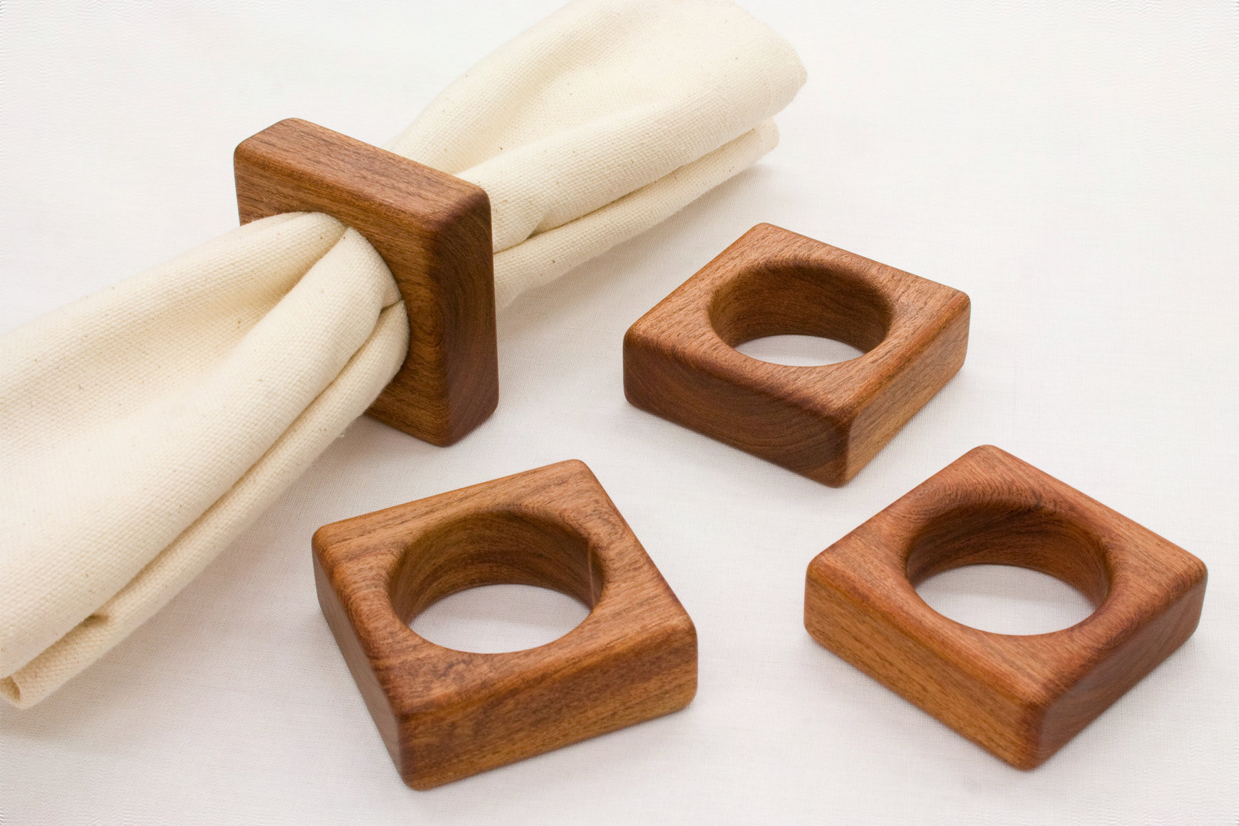 Set of 4 BYST napkin rings in Mesquite arranged on a table linen; one ring holds a cloth napkin